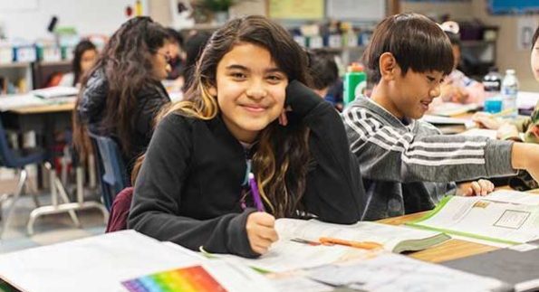 girl smiling at camera in classroom while writing