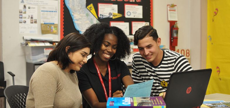 three students looking at a laptop in a classroom